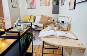 Un salon chaleureux avec une table basse en bois, un canapé avec des coussins, une table d’appoint avec une machine à café et une bibliothèque.