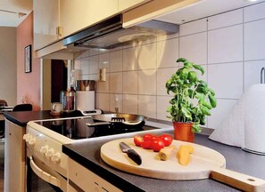 A modern kitchen with a stove, a cutting board with vegetables, and a potted basil plant. - Heart of Bergen, Great view from patio, Renovated (Bergenhus)