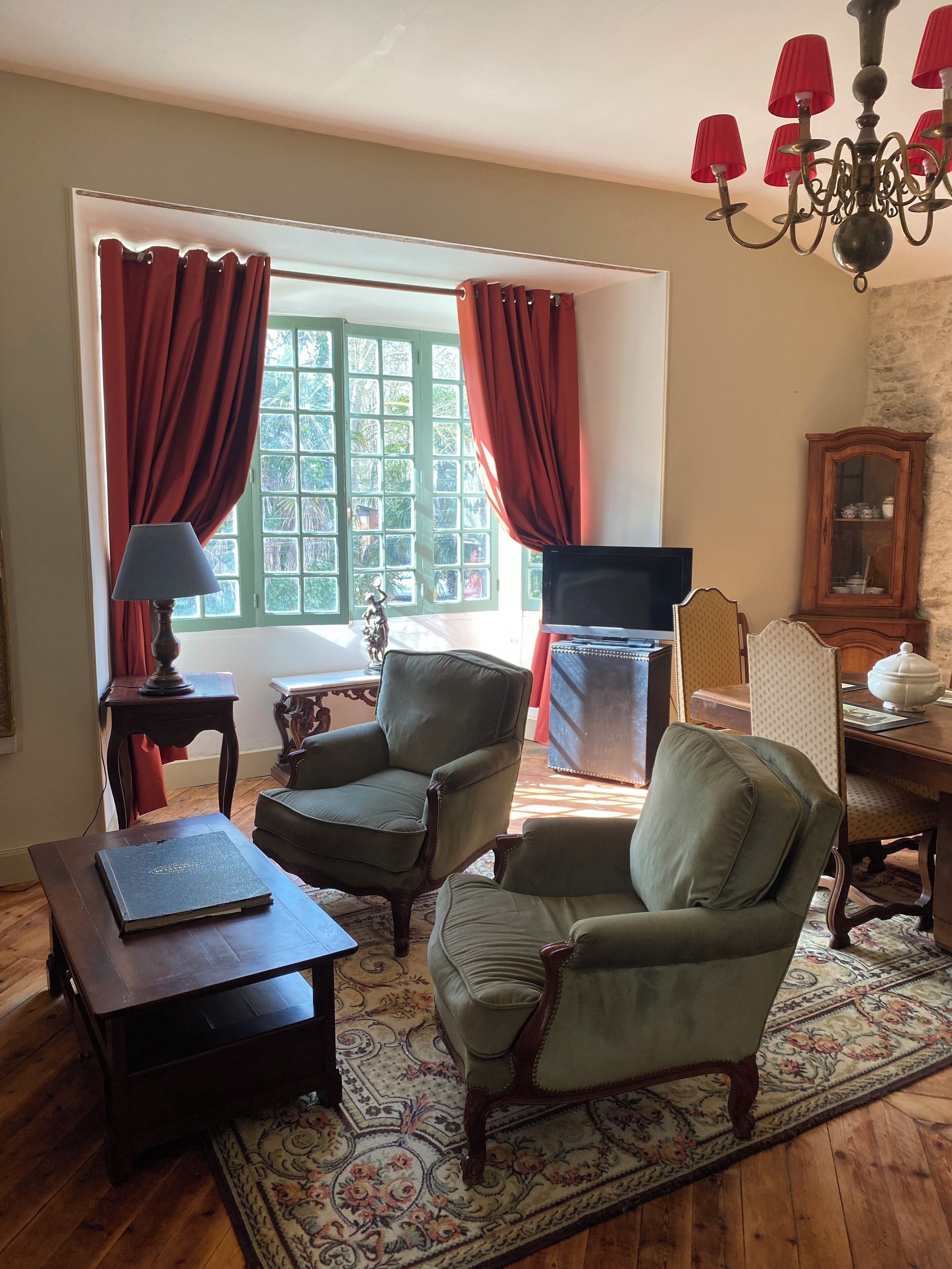Un salon traditionnel avec deux fauteuils, une petite table, un téléviseur et un lustre.