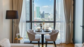 A room with a large window, a dining table with two chairs, a lamp, and a framed picture on a small table. - Bangkok Luxury New Condo · Siam Paragon · Walk to BTS (Bangkok)