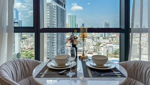 A dining table with two bowls, a wine glass, and cutlery set against a cityscape view through large windows. - Bangkok Luxury New Condo · Siam Paragon · Walk to BTS (Bangkok)