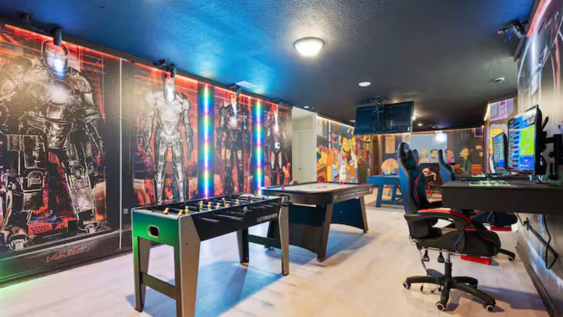 A room with a foosball table, a desk with a computer, and a colorful mural on the wall.