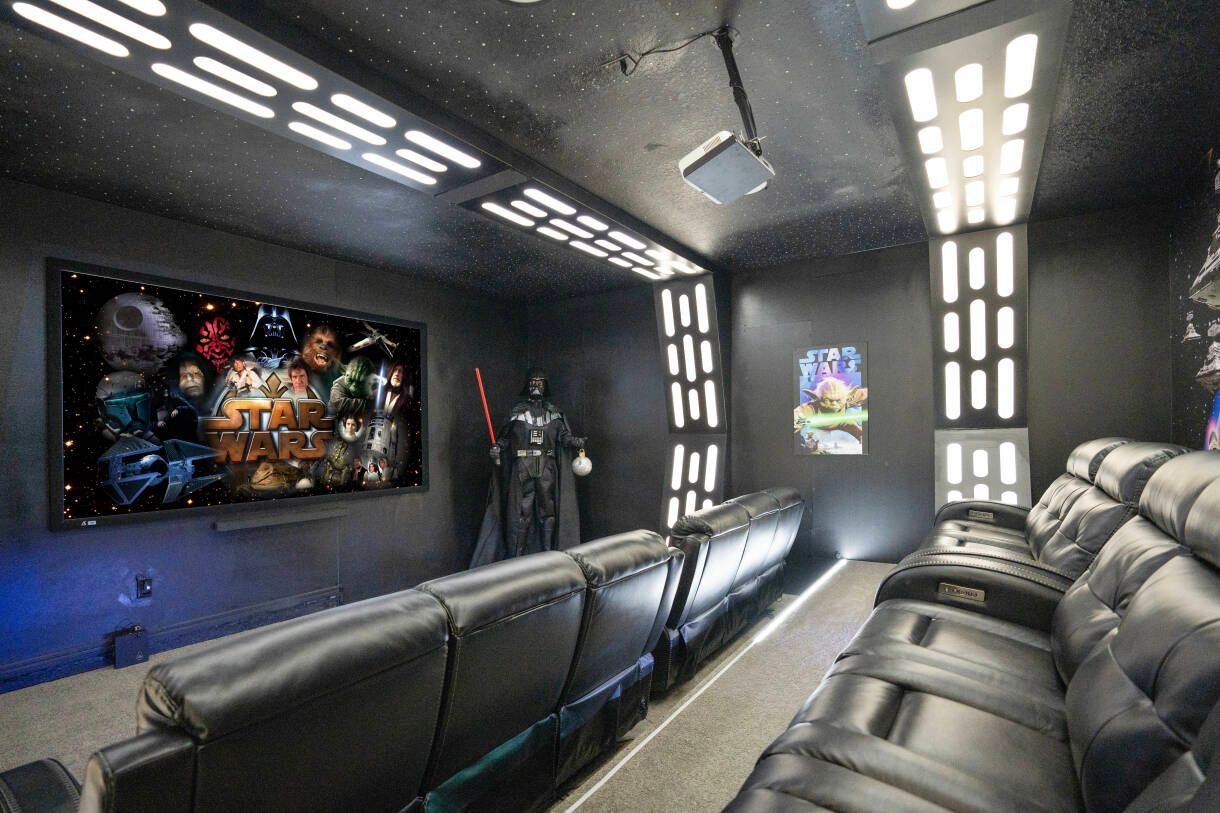 Ein Kinoraum mit schwarzen Ledersesseln, einer großen Leinwand, die einen Star Wars Film zeigt, und Star-Wars-Dekoration.