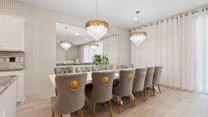 A modern dining room with a long table, six chairs with gold accents, and two chandeliers. - 10br Villa w/ Star Wars Theater & Game Room (Davenport)