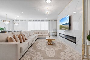A modern living room with a sectional sofa, a flat-screen TV mounted on the wall, and a decorative rug. - 10br Villa w/ Star Wars Theater & Game Room (Davenport)