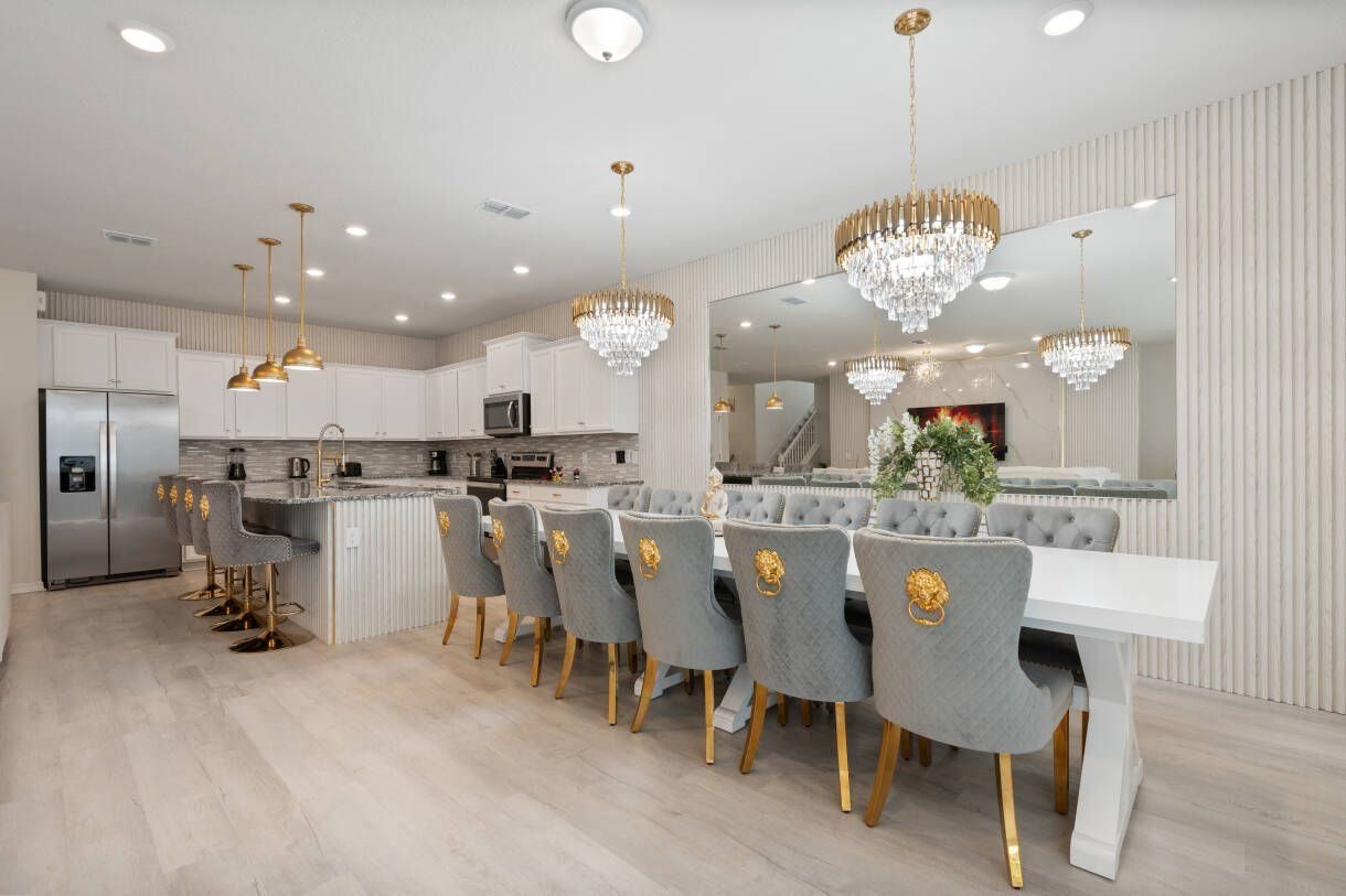 A modern kitchen with a central island, bar seating, and a dining area with a large mirror and chandelier.