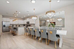 A modern kitchen with a central island, bar seating, and a dining area with a large mirror and chandelier. - 10br Villa w/ Star Wars Theater & Game Room (Davenport)