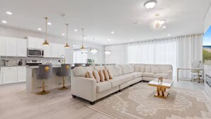 A modern kitchen with white cabinets and stainless steel appliances, a large L-shaped sectional sofa, and a dining area with a glass table. - 10br Villa w/ Star Wars Theater & Game Room (Davenport)