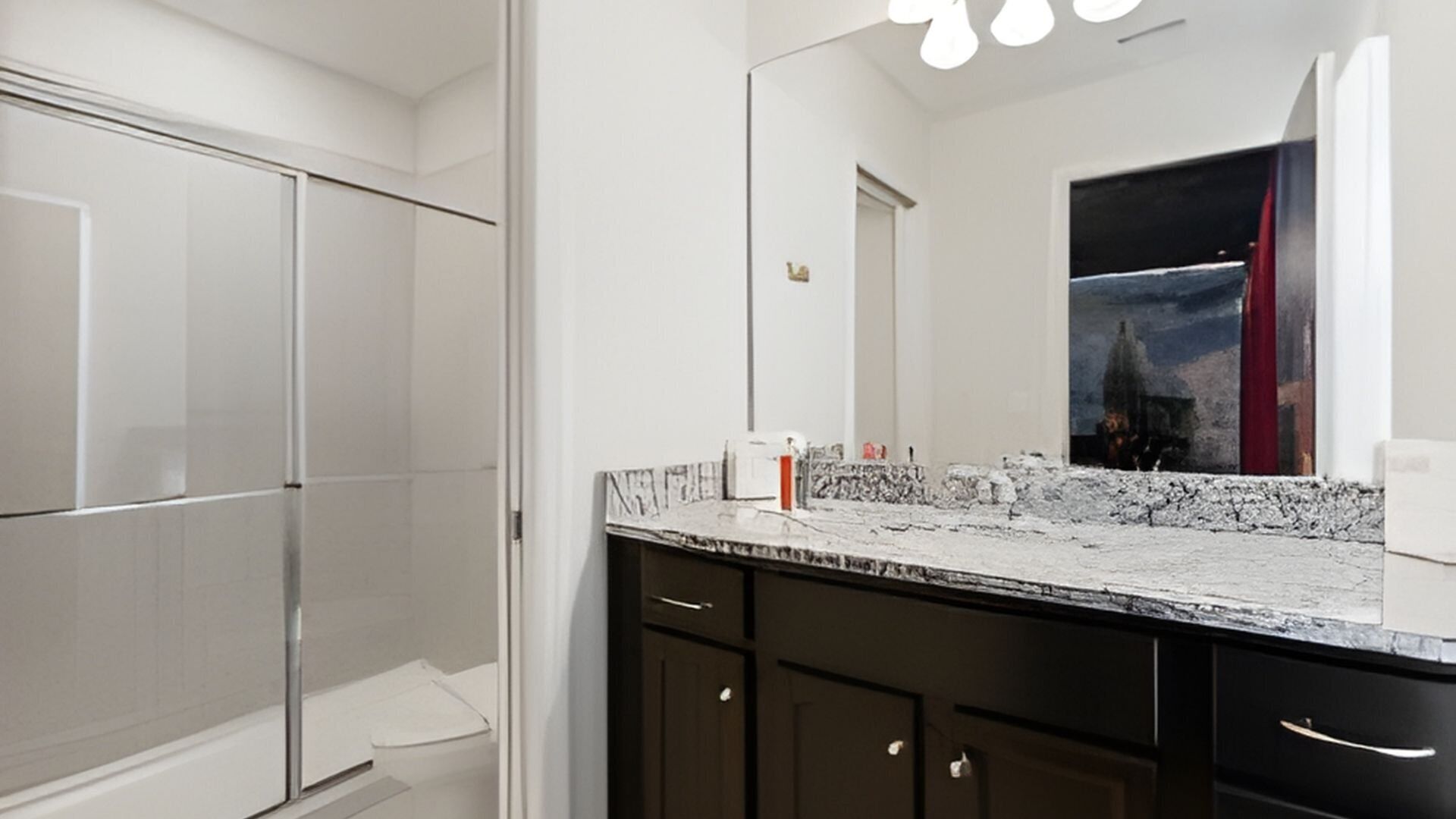 A modern bathroom with a large mirror, dark cabinets, and a marble countertop.