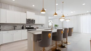 A modern kitchen with white cabinetry, a central island, and pendant lighting. - 10br Villa w/ Star Wars Theater & Game Room (Davenport)