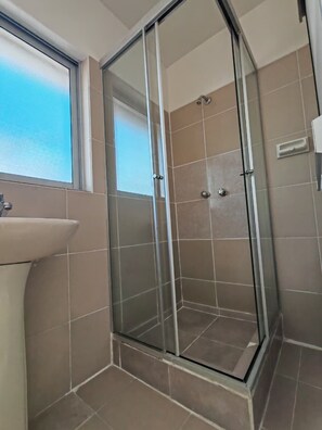A bathroom with a glass shower enclosure, a sink, and a window. - YORK HOSTEL (La Paz)