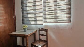 A room with a bed, a wooden desk, a chair, and a window with blinds.
