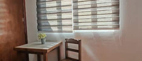 A room with a bed, a wooden desk, a chair, and a window with blinds.