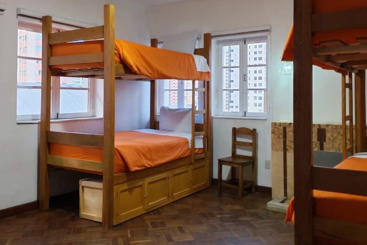 A bunk bed room with a wooden floor, a window, and a chair.