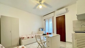 A compact room with a bed, a desk, a chair, a ceiling fan, a microwave, and a window. - Studio With Balcony Close to the Beach (Caorle)