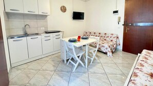 A compact kitchen with white cabinets, a sink, and a dining area with a table and chairs. - Studio With Balcony Close to the Beach (Caorle)