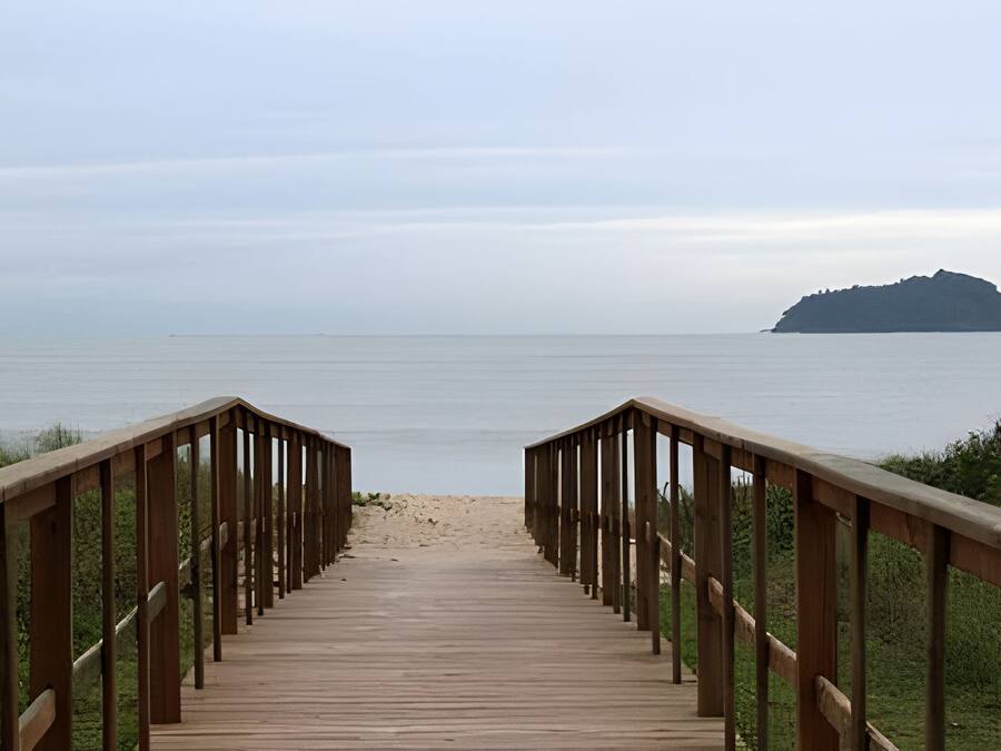 Una pasarela de madera que lleva a una playa con vistas al mar y una isla distante.