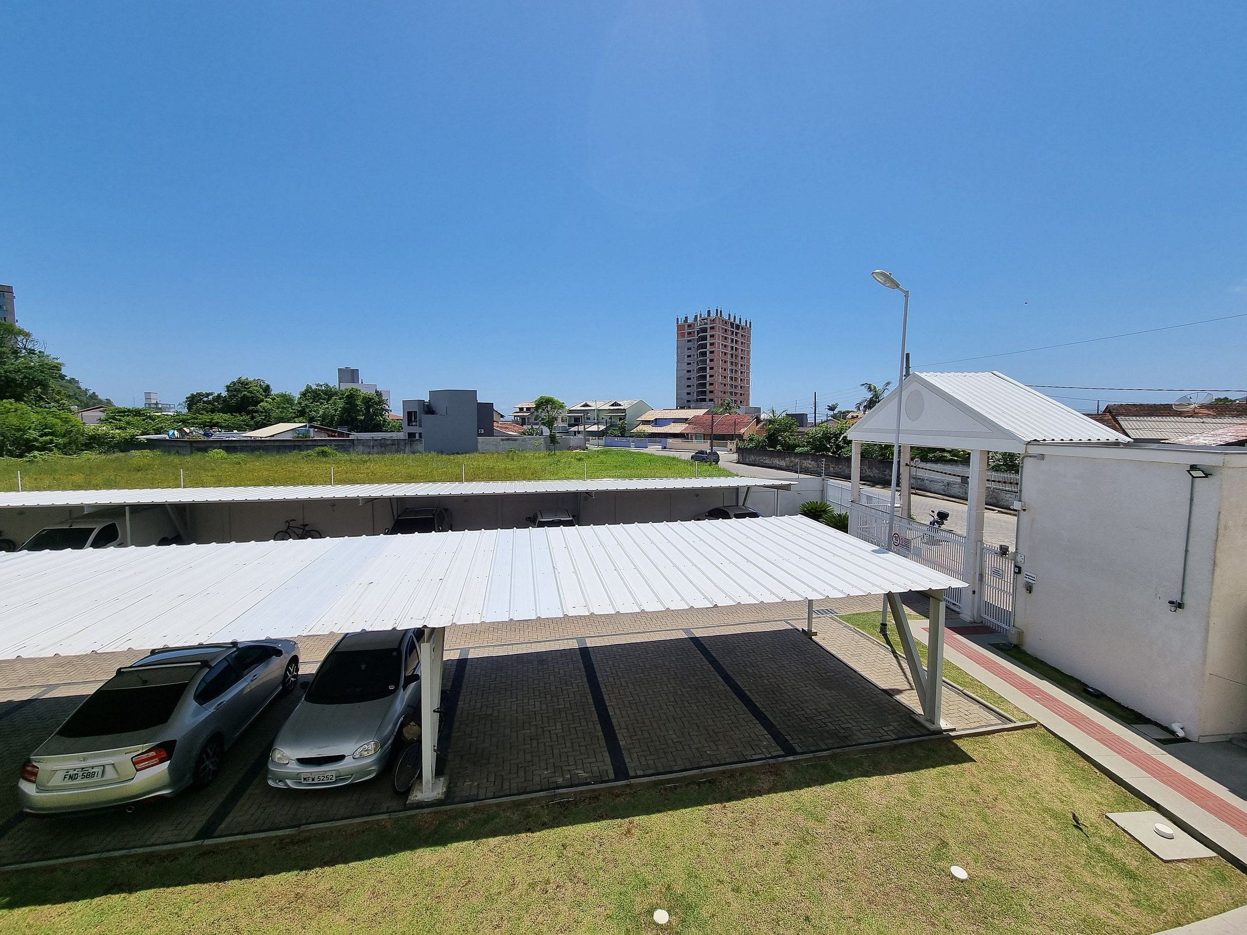 Un estacionamiento con dos autos, una zona de espera techada y un edificio alto al fondo.