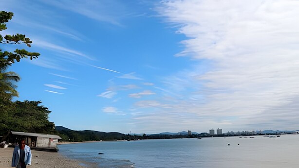 Una playa con cielo despejado, agua tranquila y edificios a lo lejos.