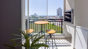 A balcony with two small tables and chairs, a potted plant, and a view of a cityscape. - Curta Praia do Quilombo - Palladium  (Penha)