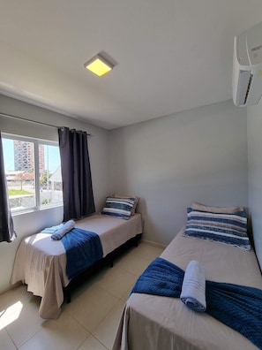 A room with two beds, a window with curtains, a ceiling light, and an air conditioning unit. - Curta Praia do Quilombo - Palladium  (Penha)