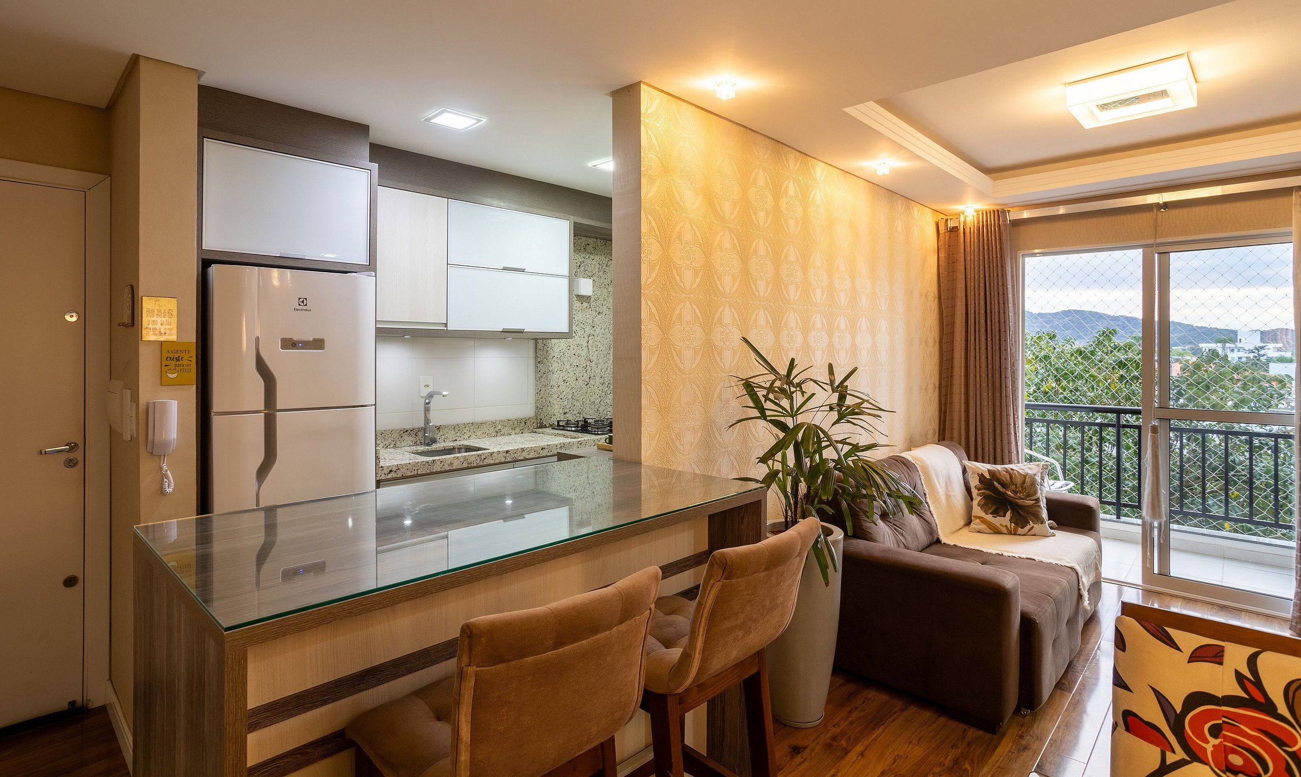 Una cocina moderna con una isla de vidrio, un comedor con dos sillas, un sofá y un balcón con vistas.
