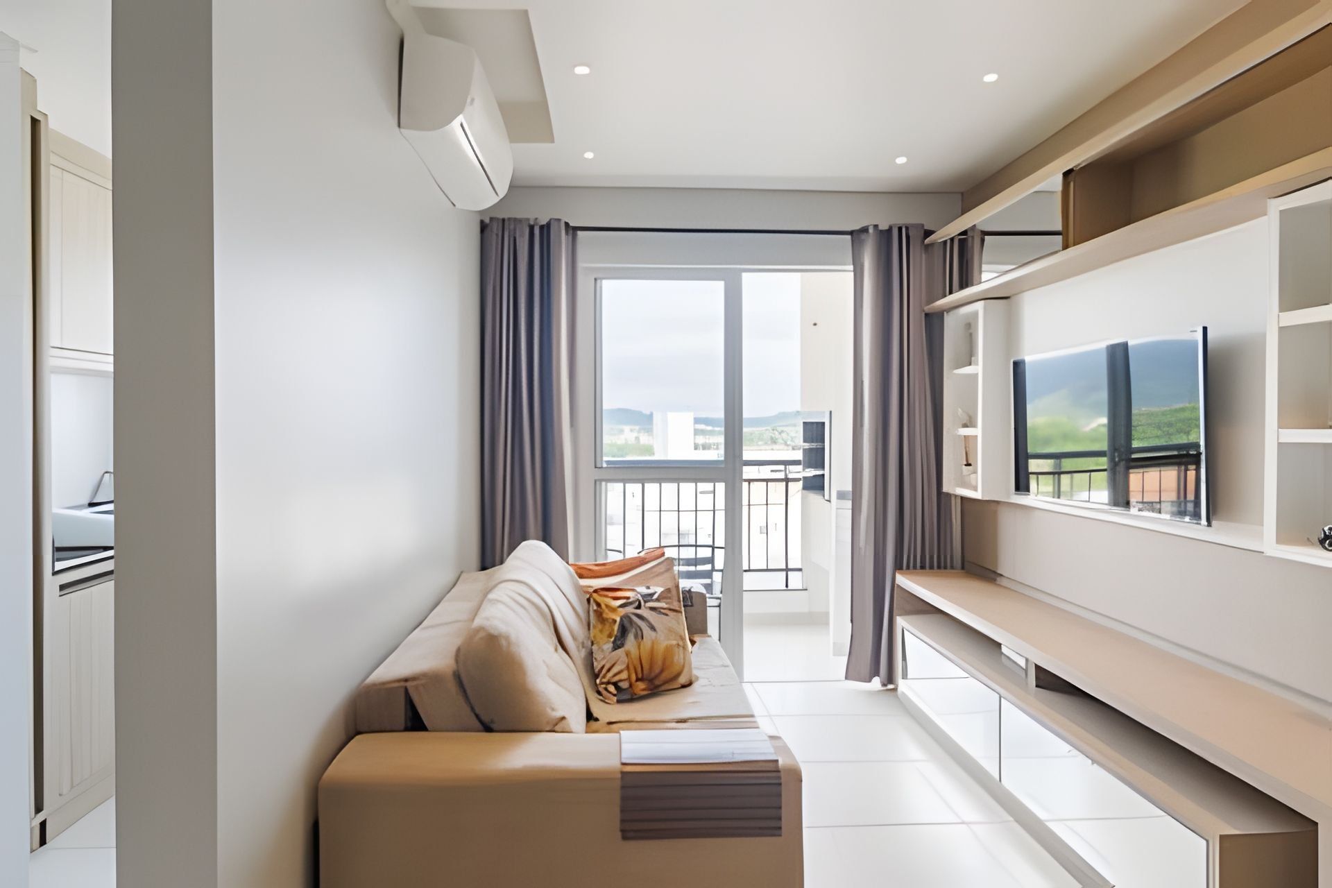 A modern living room with a sofa, a flat-screen TV, and a balcony with a city view.