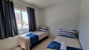 Una habitación pequeña y limpia con dos camas, una ventana con cortinas y vistas a edificios.