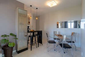 A modern kitchen with a dining area, including a glass table and chairs, a refrigerator, and a hanging light fixture. - Curta Praia do Quilombo - Palladium  (Penha)