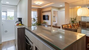 Una cocina moderna con una isla de vidrio, un rincón de comedor con un sofá y una sala de estar con televisor y plantas.