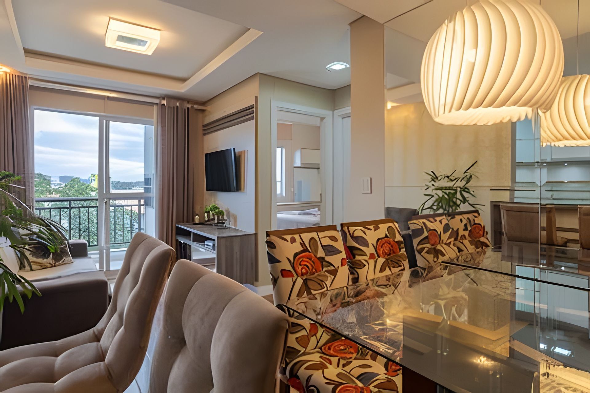 A modern living room with a sofa, a glass dining table, and a TV mounted on the wall.