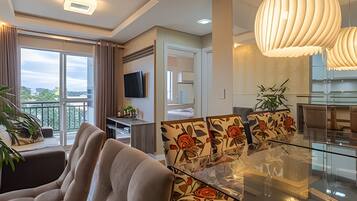 A modern living room with a sofa, a glass dining table, and a TV mounted on the wall.