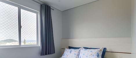 Een slaapkamer met een bed, een raam met gordijnen en een nachtkastje.