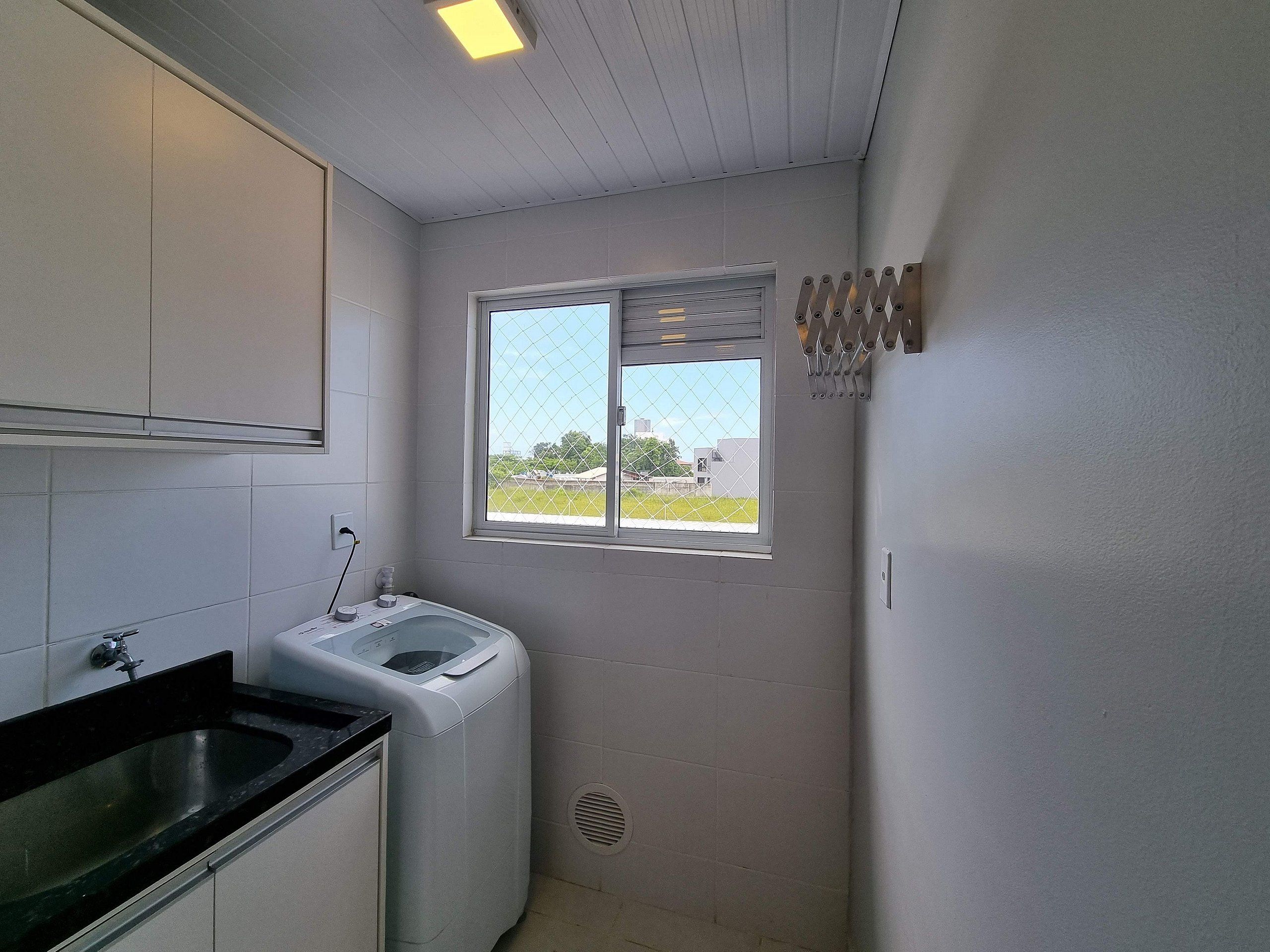 A compact kitchen with a washing machine, a sink, and a window with a view of the outside.