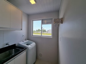 A compact kitchen with a washing machine, a sink, and a window with a view of the outside. - Curta Praia do Quilombo - Palladium  (Penha)