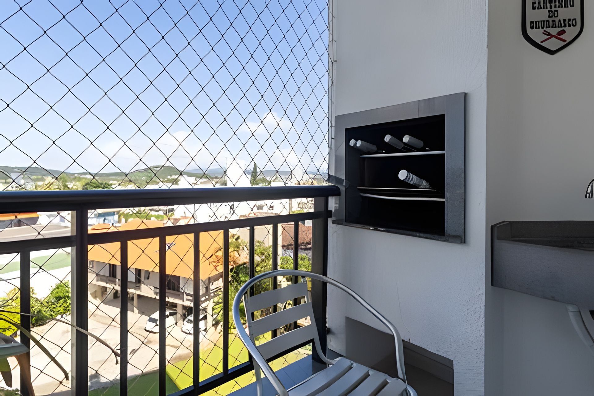 A balcony with a metal railing, a white chair, and a wall-mounted grill.