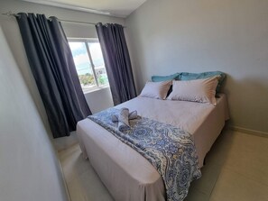 A bedroom with a bed, pillows, a blanket, and curtains.