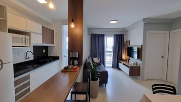 A modern kitchen with a central island, a dining area with a sofa, and a living space with a TV and a plant.