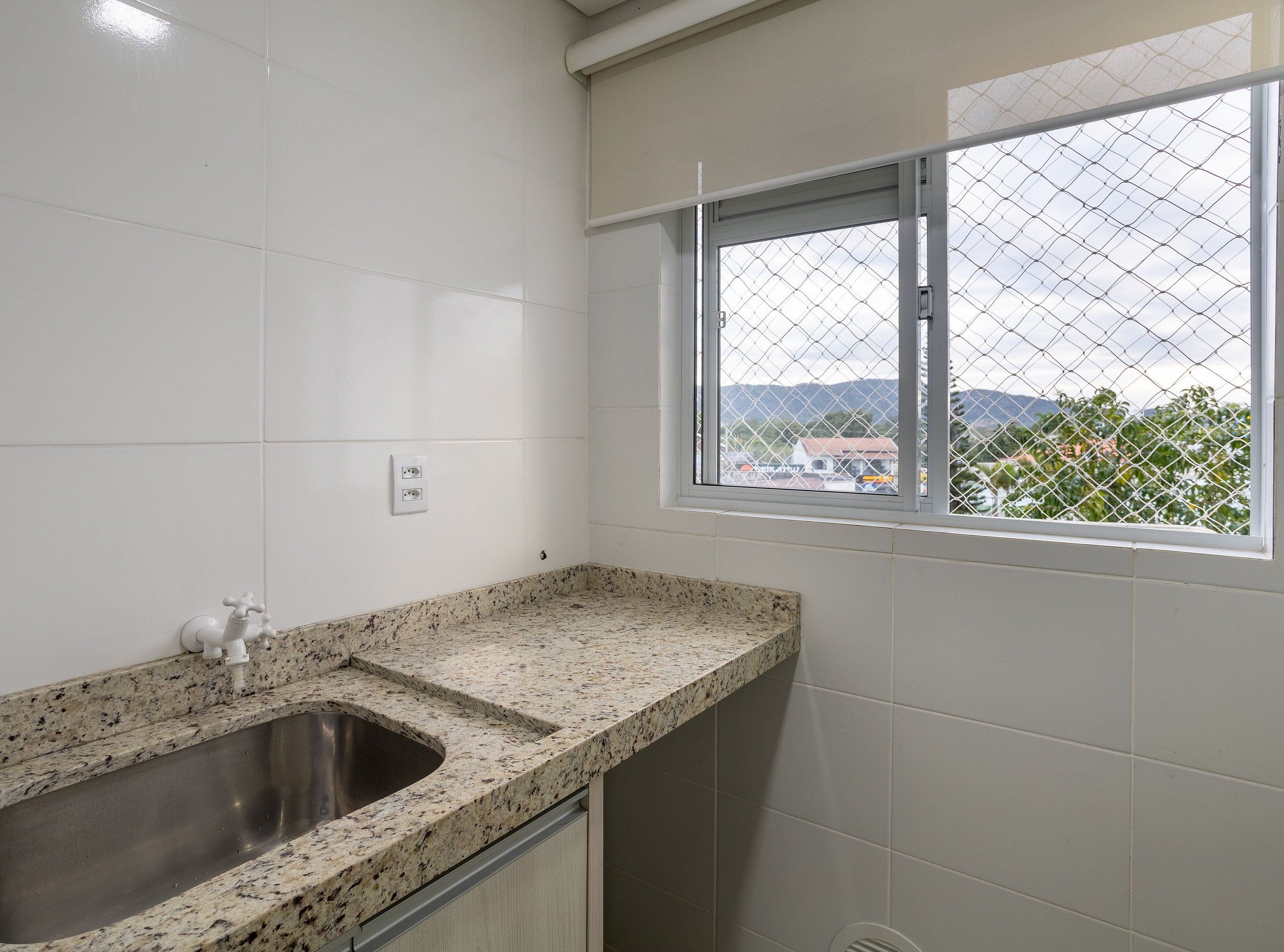 Una cocina con encimera de granito, pileta de acero inoxidable y ventana con vistas al exterior.