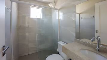 A modern bathroom with a glass shower enclosure, a white toilet, and a sink with a beige countertop.