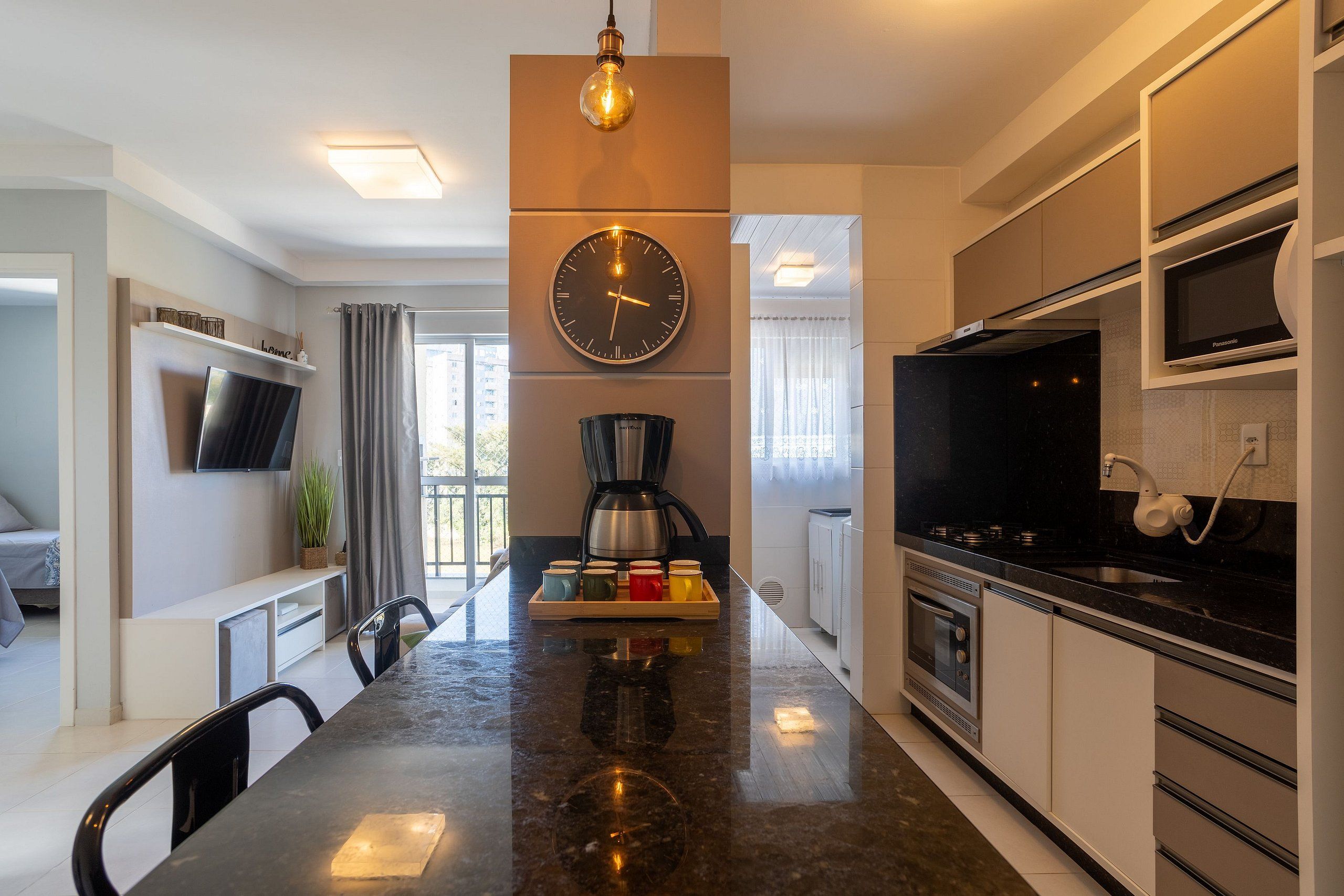 A modern kitchen with a central island, a wall-mounted clock, and a flat-screen TV.