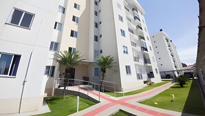 A modern multi-story residential building with balconies, a central courtyard with a red pathway, and surrounding greenery. - Curta Praia do Quilombo - Palladium  (Penha)