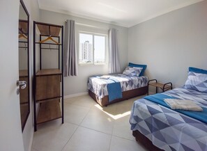 A bedroom with two beds, a wardrobe, and a window with curtains. - Curta Praia do Quilombo - Palladium (Penha)