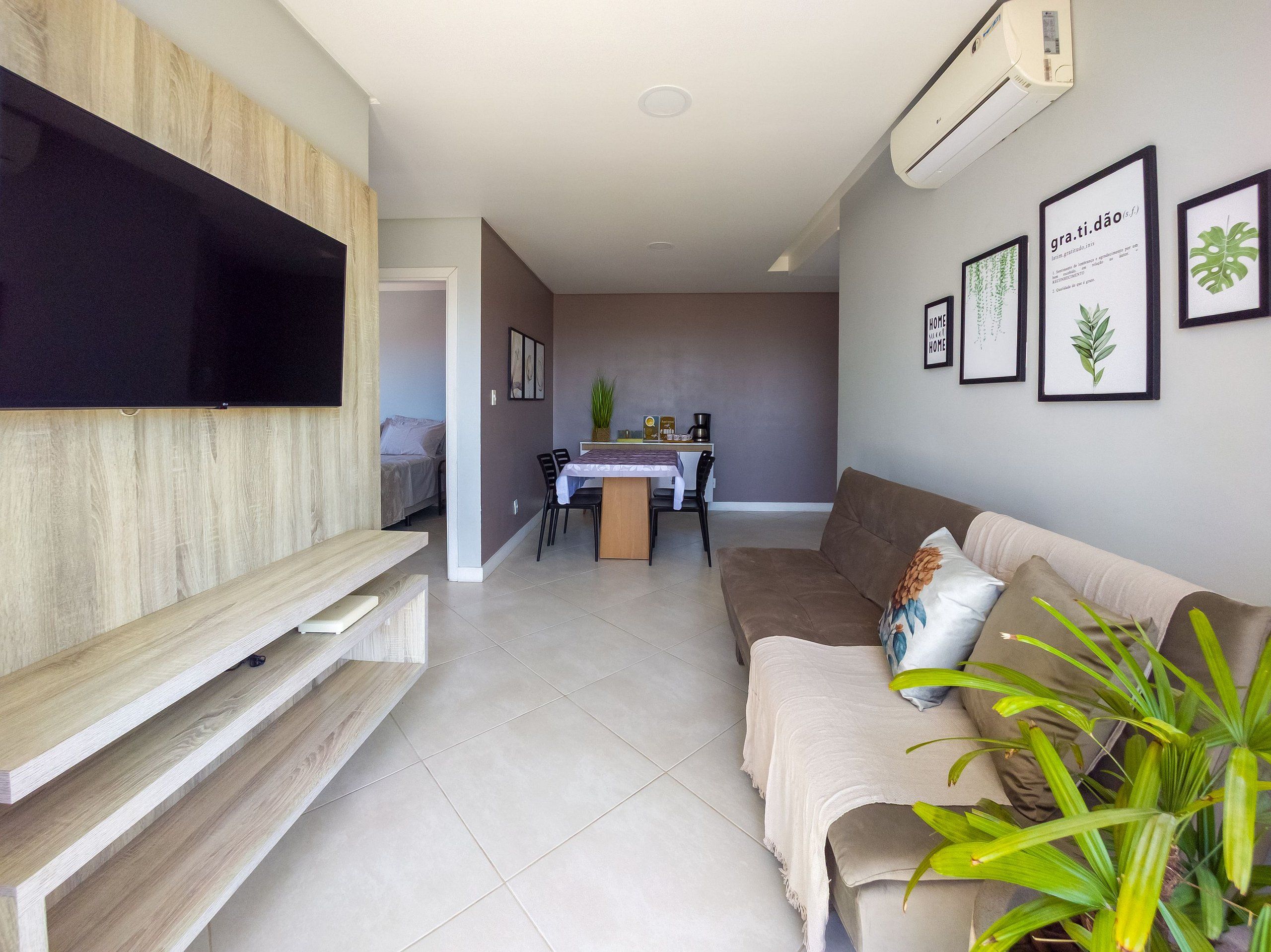A modern living room with a flat-screen TV, a sofa, a dining area with a table and chairs, and a potted plant.