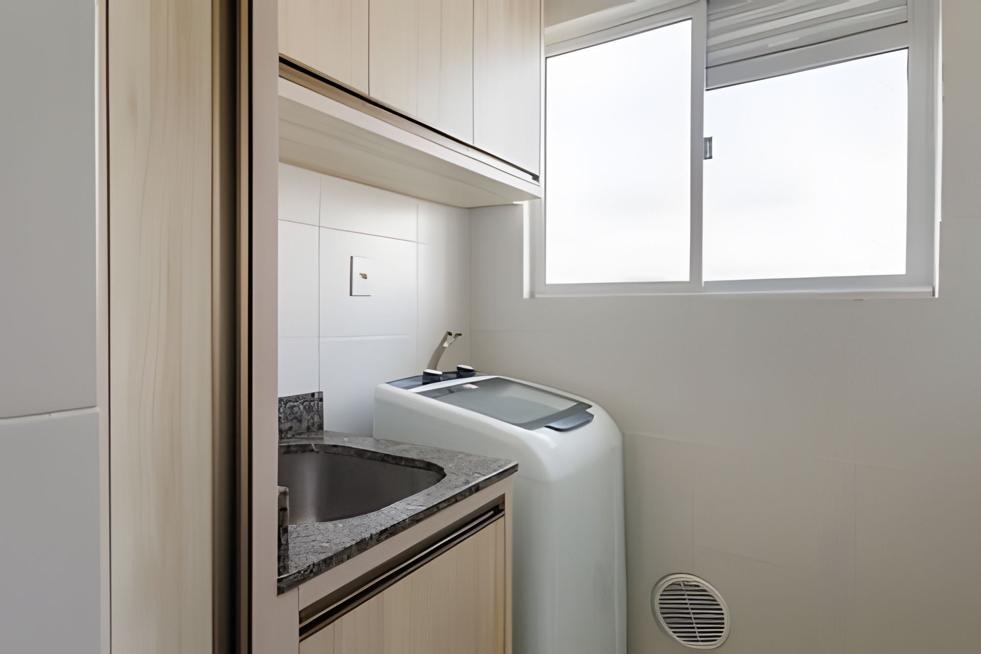 A compact kitchen with a built-in washing machine, a sink, and a window providing natural light.