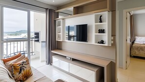 A modern living room with a large TV, built-in shelves, and a balcony with a view. - Curta Praia do Quilombo - Palladium  (Penha)