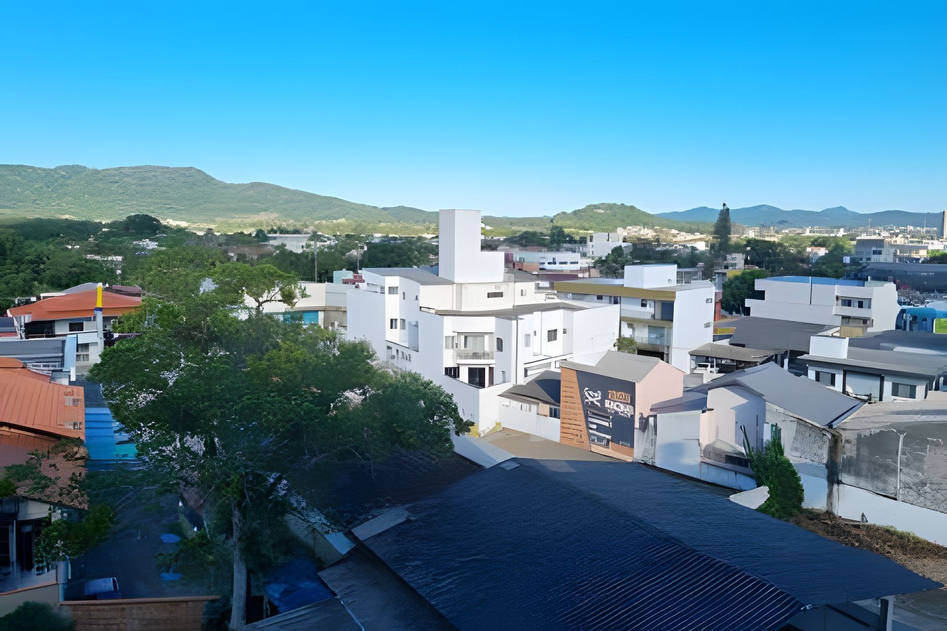 A modern urban area with white buildings, a prominent tower, and a view of distant hills.