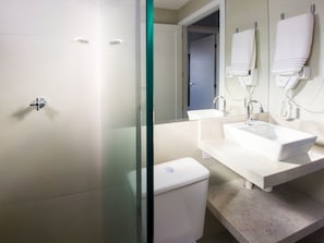 A modern bathroom with a glass shower enclosure, a white toilet, a sink with a mirror, and a towel hanging on a wall-mounted towel warmer. - Curta Praia do Quilombo - Palladium  (Penha)