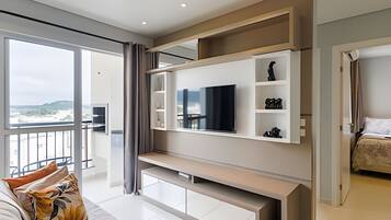 A modern living room with a large TV, built-in shelves, and a balcony with a view.