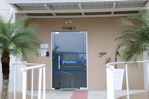 A hotel entrance with a glass door, palm trees, and a sign reading "TOUR E". - Curta Praia do Quilombo - Palladium  (Penha)